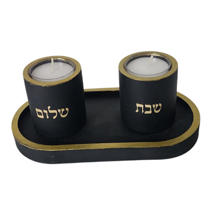 זוג פמוטים שחורים בעבודת יד עם כיתוב "שבת" ו"שלום" בצבע זהב, עשויים מבטון פולימרי, מונחים על מגש שחור עם מסגרת זהב.