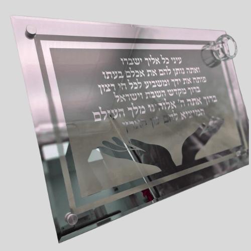 מגש חלה זכוכית עבה עם חריטה של ברכת "המוציא לחם מן הארץ" וקטע תהילים, עיטור זוג ידיים פתוחות ומוביל קטן למלח בפינה.

