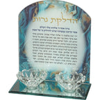 מעמד זכוכית יוקרתי להדלקת נרות שבת הכולל בסיס מראה ושני פמוטים שקופים בצורת פרח. מאחורי הפמוטים ניצב לוח זכוכית עם סיומת מעוגלת, המעוטר בדוגמת שיש מהפנטת בגווני כחול עמוק, תכלת וזהב. על הלוח מודפסת תפילת "הדלקת נרות" המלאה, כאשר הכותרת מובלטת באותיות זהב אלגנטיות.