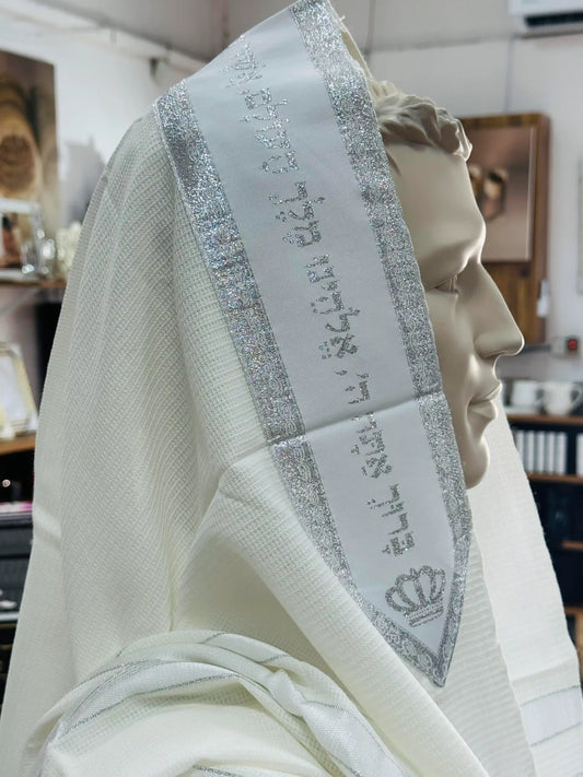 טלית לבנה מהודרת עם פס כסף ורקמת ברכת כהנים ועיטור כתר המונחת על ראש בובת תצוגה בתוך חנות יודאיקה