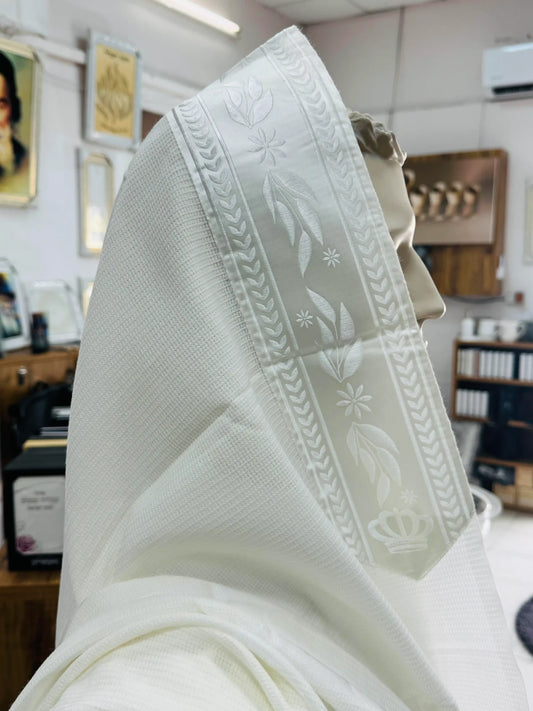 טלית לבנה עם פס דוגמת עלים ורקמה עדינה מונחת על ראש בובת תצוגה בתוך חנות יודאיקה