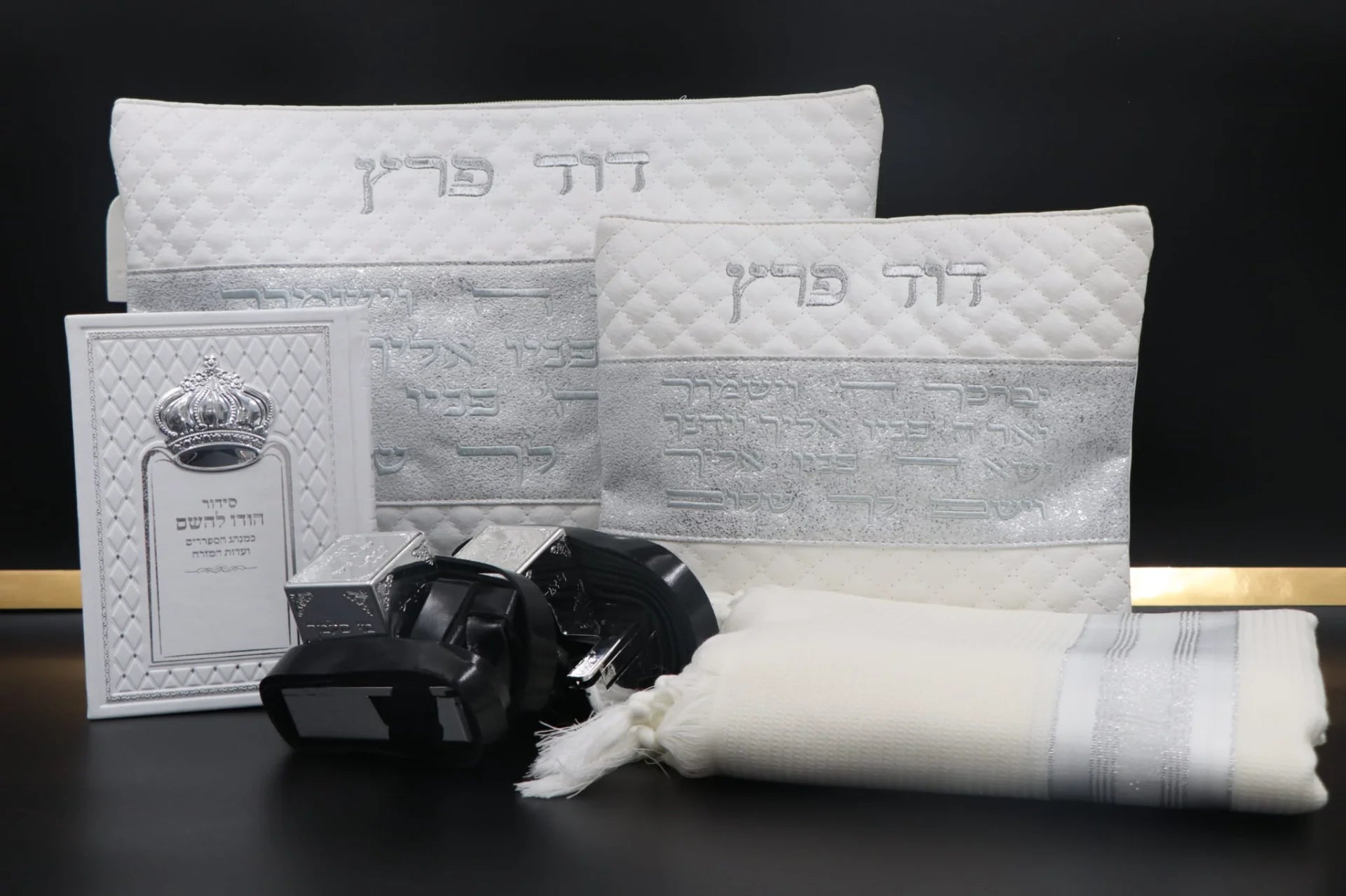 סט בר מצווה מהודר בצבע לבן וכסף הכולל תיק טלית, תיק תפילין, טלית לבנה, זוג תפילין שחורים וסידור תפילה על רקע כהה