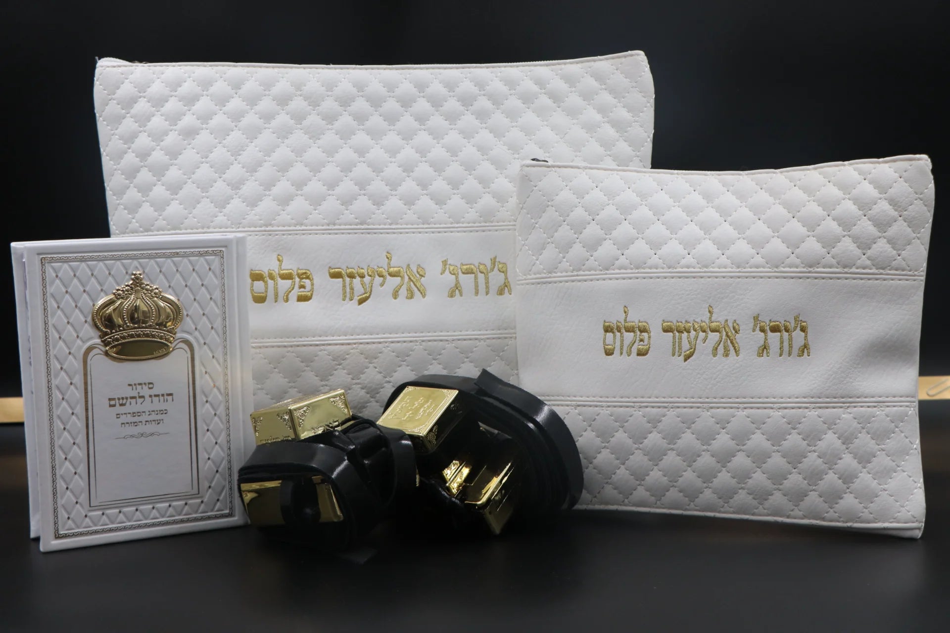 סט בר מצווה מהודר בצבע לבן וזהב הכולל תיק טלית, תיק תפילין, זוג תפילין שחורים עם בתי זהב וסידור תפילה בעיצוב כתר על רקע כהה