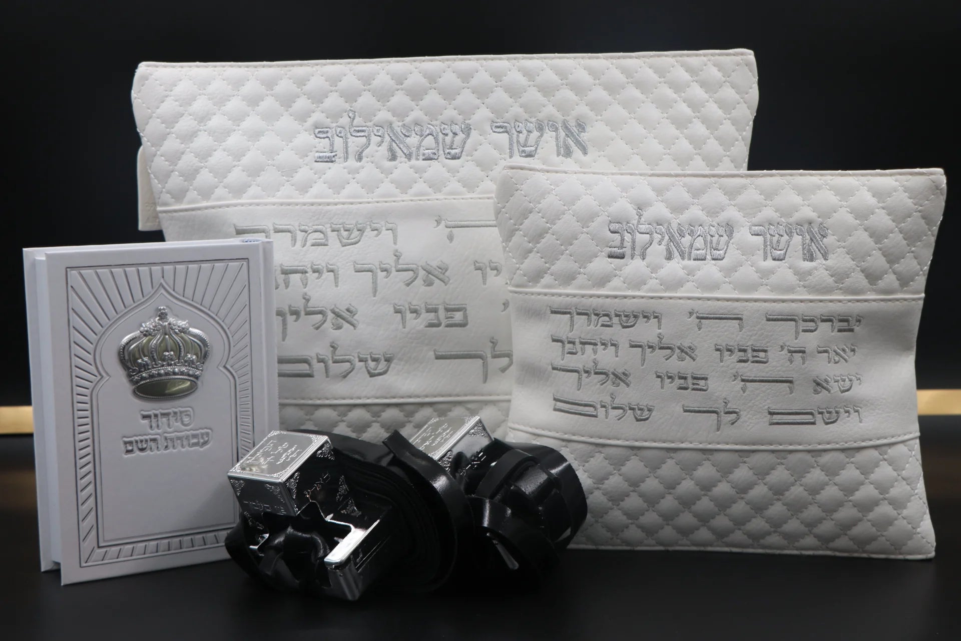 סט בר מצווה מהודר בצבע לבן וכסף הכולל תיק טלית, תיק תפילין עם רקמת שמות, זוג תפילין שחורים עם בתי כסף וסידור תפילה בעיצוב כתר על רקע כהה