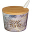 כלי עגול לדבש עשוי מלמין בגובה 6.5 ס"מ בדוגמת שיש בגווני סגול ואפור, עם כיתוב מוזהב "שנה טובה", מכסה עץ במבוק וכפית חרסינה לבנה.